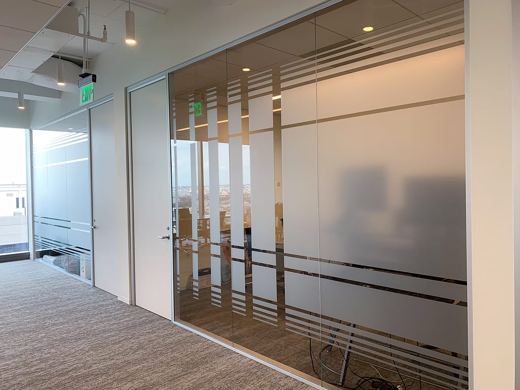 Offices with wood doors and glass walls. The glass has a frosted or etched vinyl film applied to it in a striking modern lined design.