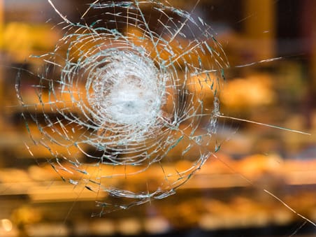 A piece of glass with damage from a baseball bat. The glass has safety window film on it so the glass is still intact and safe.
