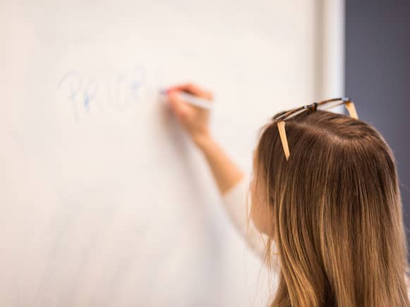 Girl with sunglasses on top of her head writing on dry erase wall vinyl.