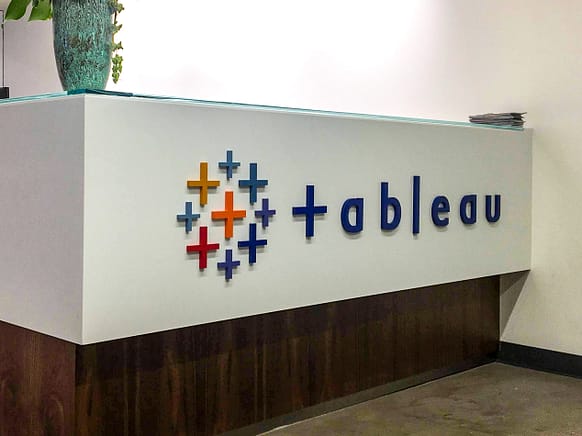 1/4" thick flat cut acrylic sign mounted to the face of a reception desk. The sign has a multicolored logo and the text "tableau".
