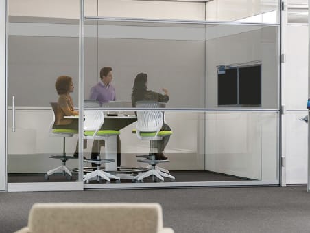 3 people in a conference room. The wall of the room is glass and has had Caper Cloaking window film applied to it in order to obscure data on the monitor mounted on the wall.